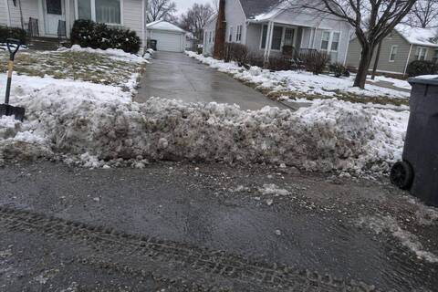 A ridge of dirty compacted snow packed across the end of a residential driveway where it meets the street, the cleared concrete stopping at the ridge