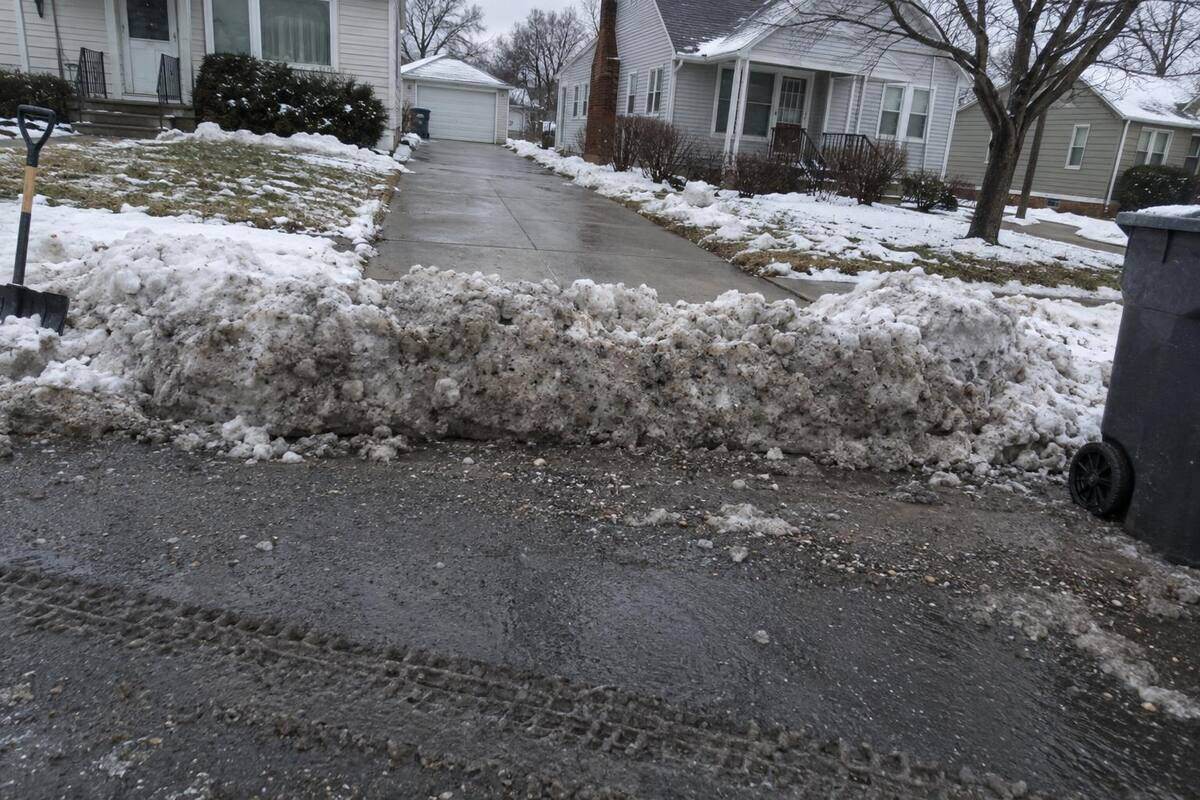 A ridge of dirty compacted snow packed across the end of a residential driveway where it meets the street, the cleared concrete stopping at the ridge